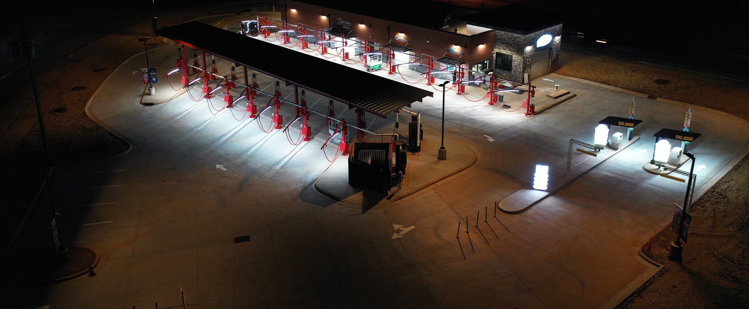 The Tiger Xpress lot at night from above: red vacuum arches under the canopy and the lit pay stations