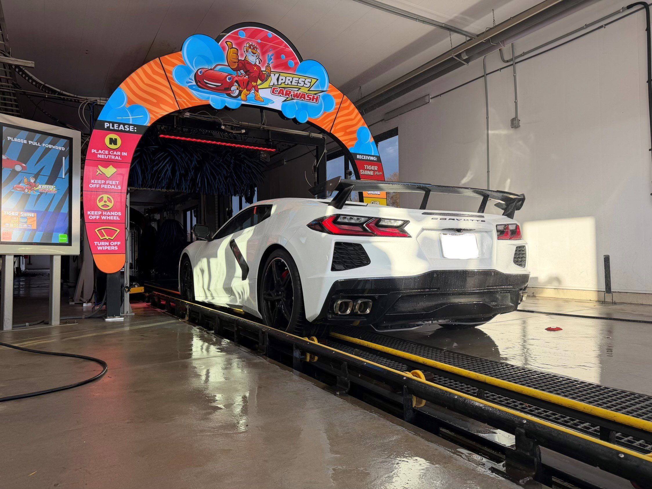 A white Corvette rolling onto the conveyor under the Tiger Xpress entrance arch