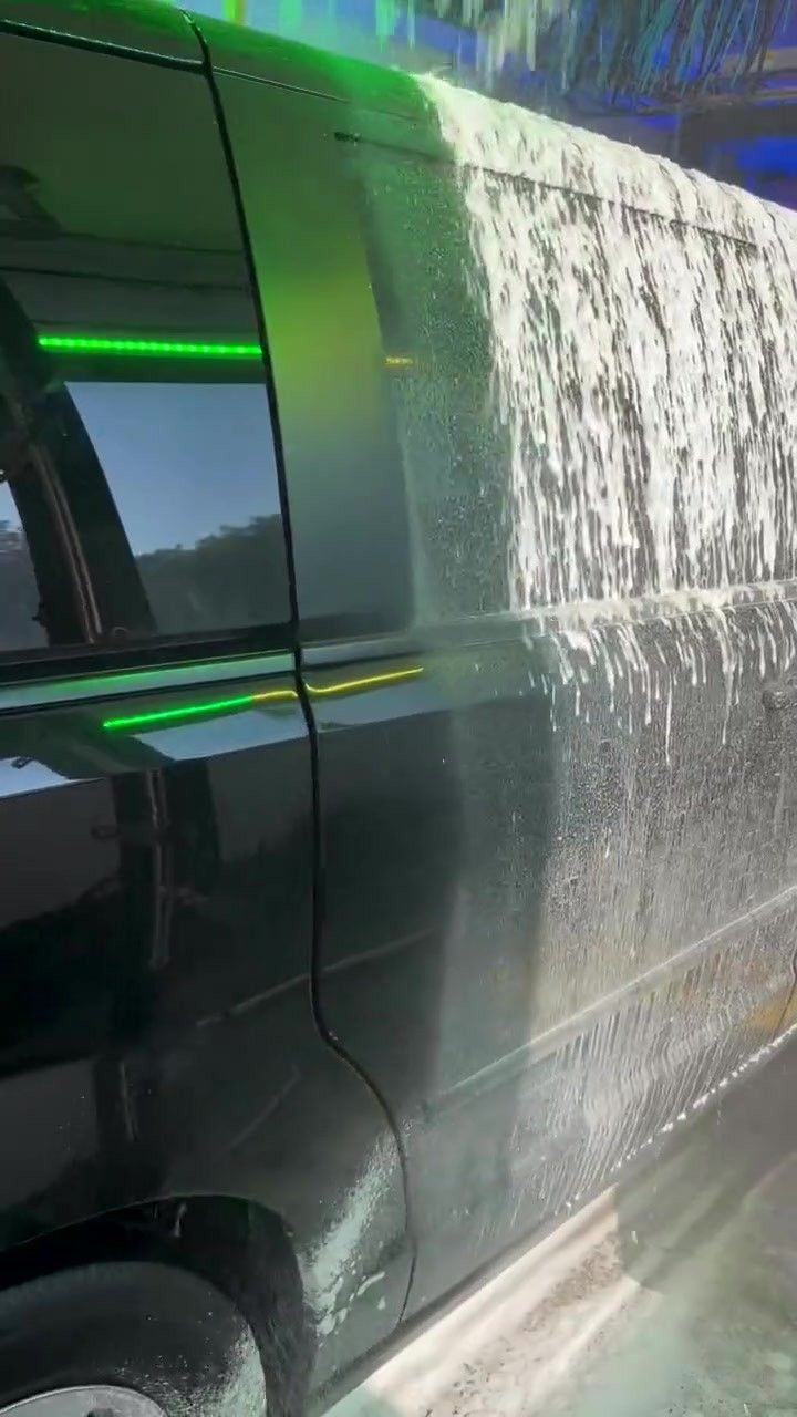 Teal wrap brushes and foam scrub a car in the tunnel